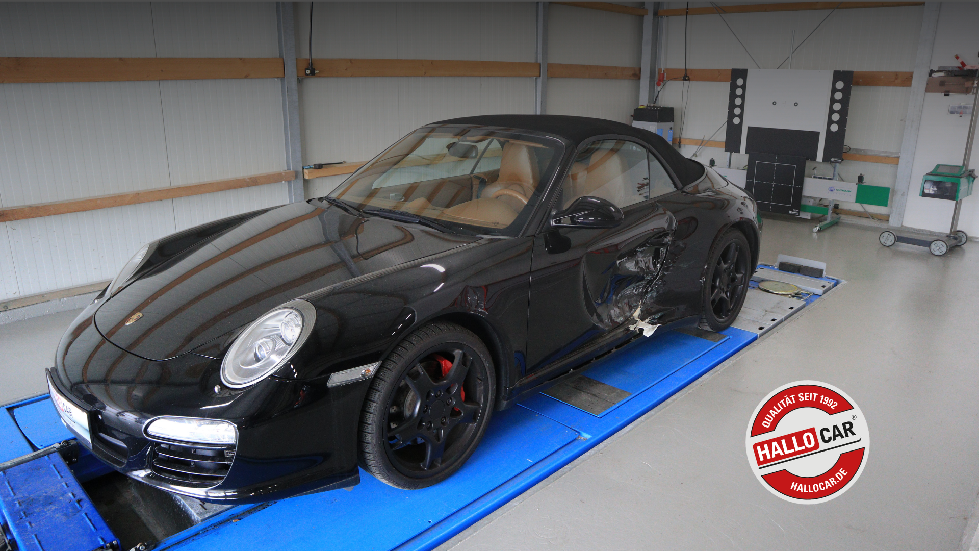 Schwarzer Porsche mit braunem Innenraum, geparkt in einer Werkstatt auf einer blauen Hebebühne, sichtbare Beschädigung an der rechten Fahrzeugseite