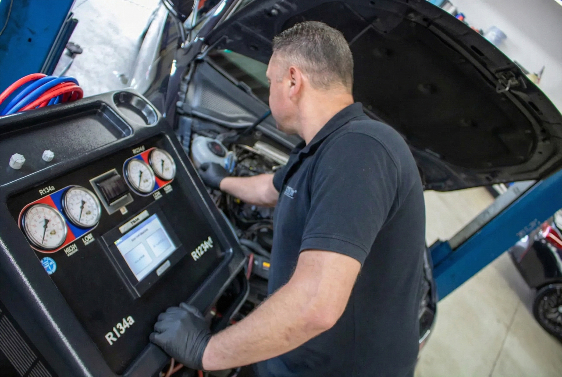 Mann mit schwarzen Handschuhen bedient Diagnosegerät neben offenem Motorhaube im Autowerkstatt.