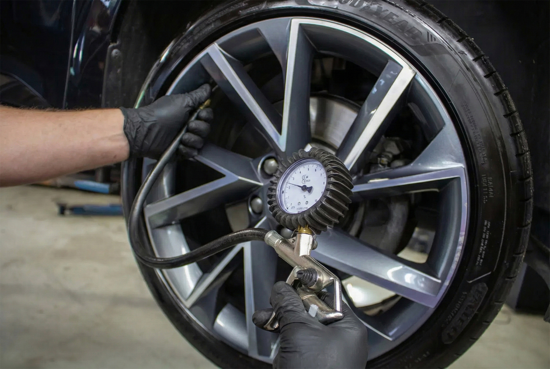Nahaufnahme von Händen mit schwarzen Handschuhen, die den Reifendruck eines Pkw-Reifens mit einem Manometer messen
