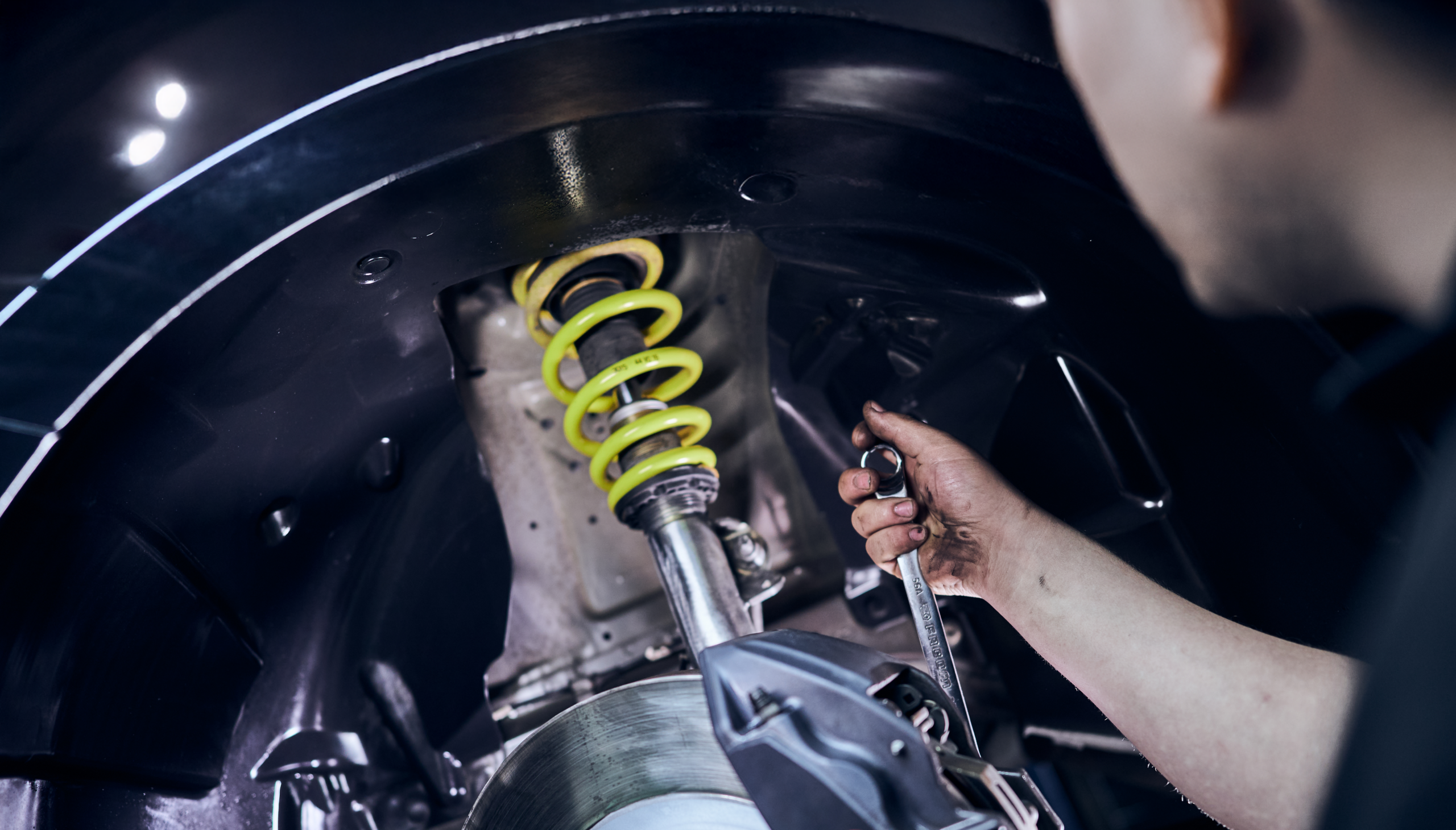 Automechaniker montiert oder repariert Stoßdämpfer und Radaufhängung mit gelber Feder am Fahrzeug.